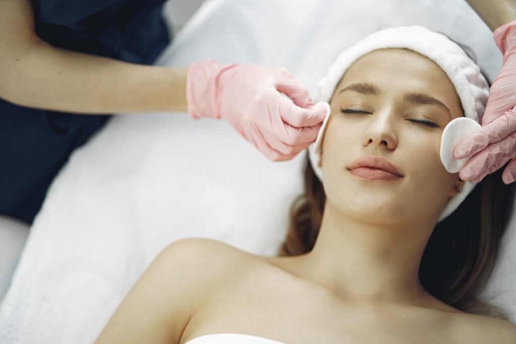Woman lying down on a beauty bed with her eyes closed getting a facial done by a beauty therapist.